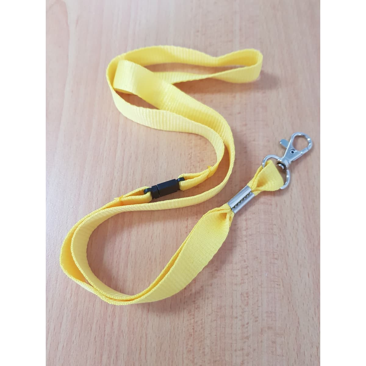 A yellow lanyard with a clip and a plastic buckle, laid out on a wooden surface.