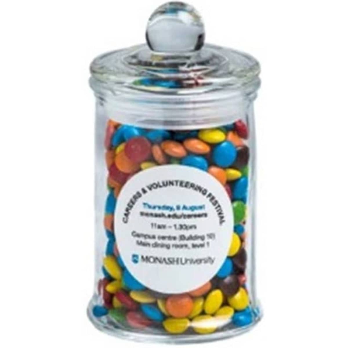 A small glass apothecary jar filled with colourful chocolate beans, featuring a round lid and a logo.