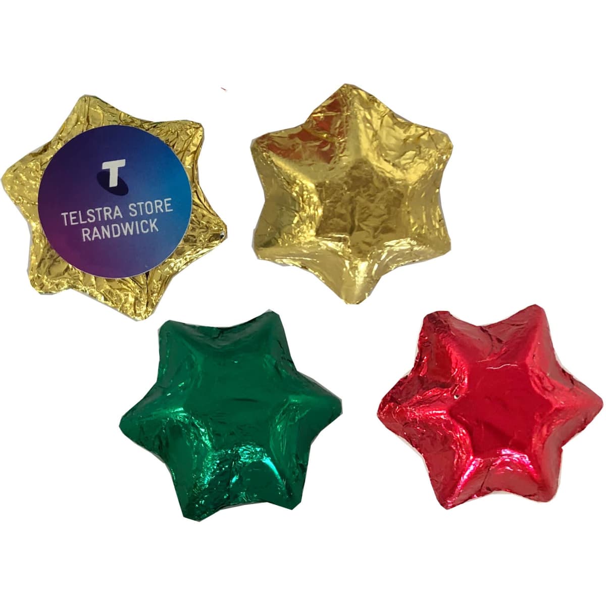 Four star-shaped chocolates wrapped in gold, green, and red foil, with a branding logo on one.
