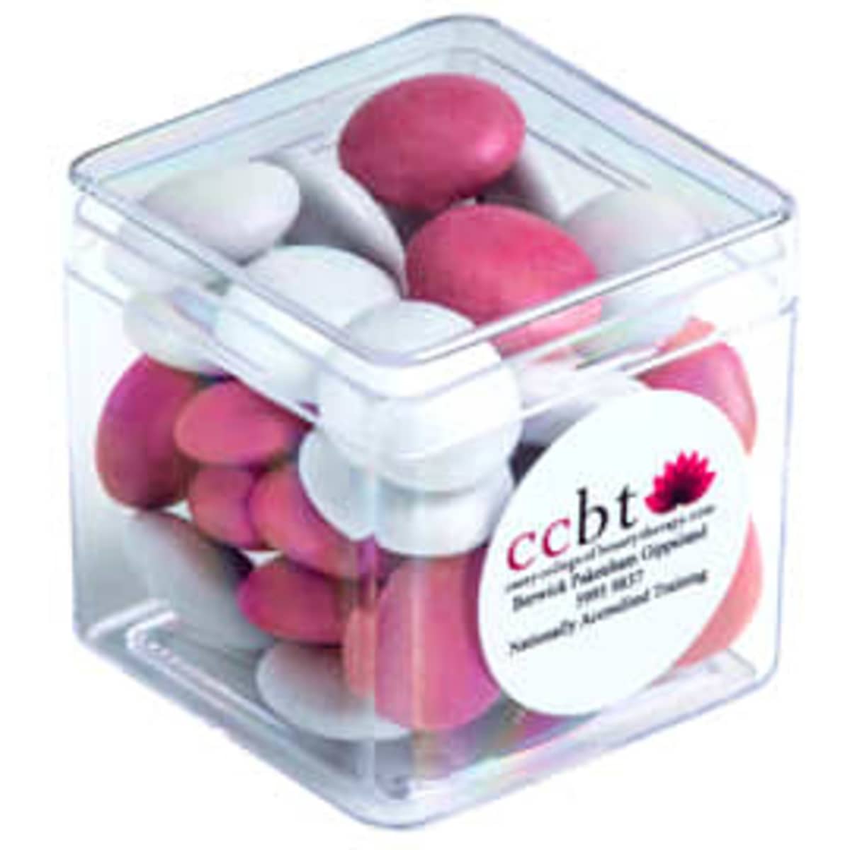 A clear cube container filled with pink and white chocolate-coated beans. The container has a label and branding.