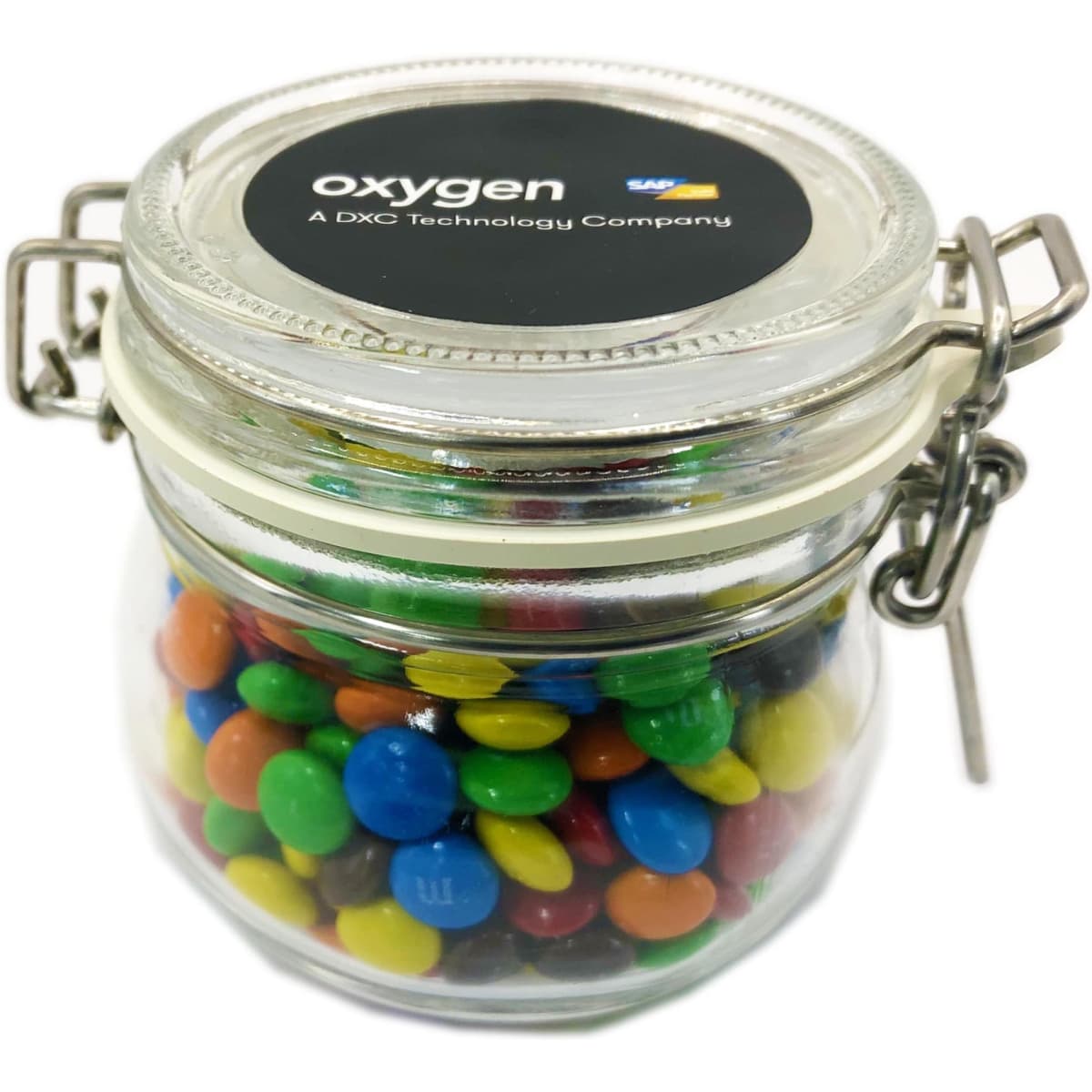 A glass canister filled with colourful mini M&Ms, featuring a metal clasp and a logo on the lid.