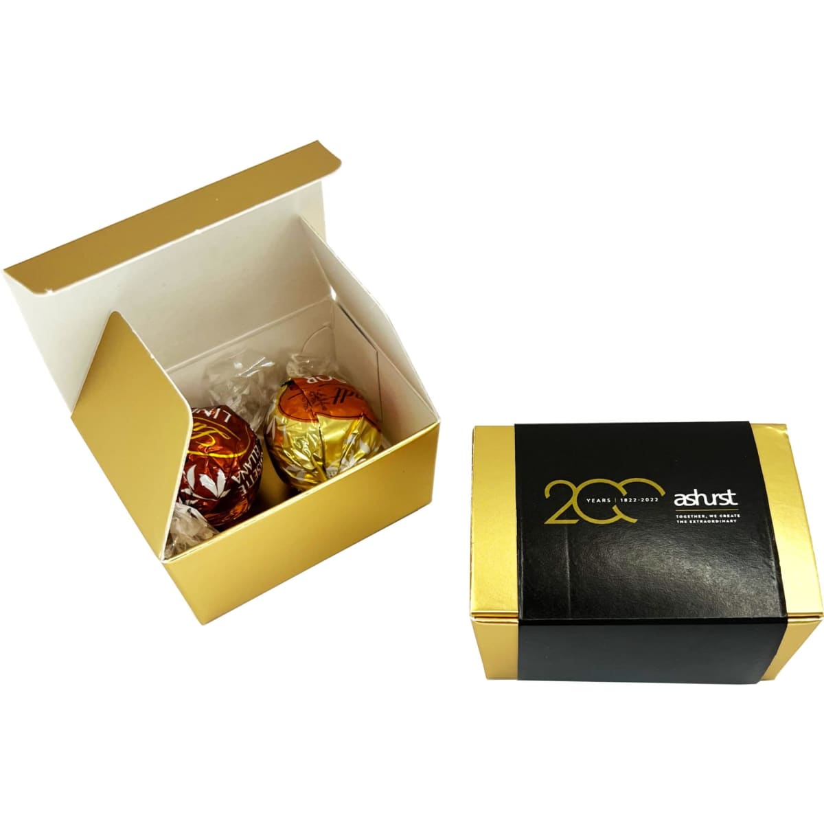 A gold and white box containing two chocolate balls, featuring branding on the exterior.