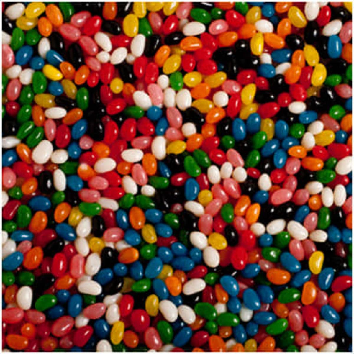 A variety of mini jelly beans in vibrant colours, including red, green, blue, black, orange, pink, and white, scattered together.