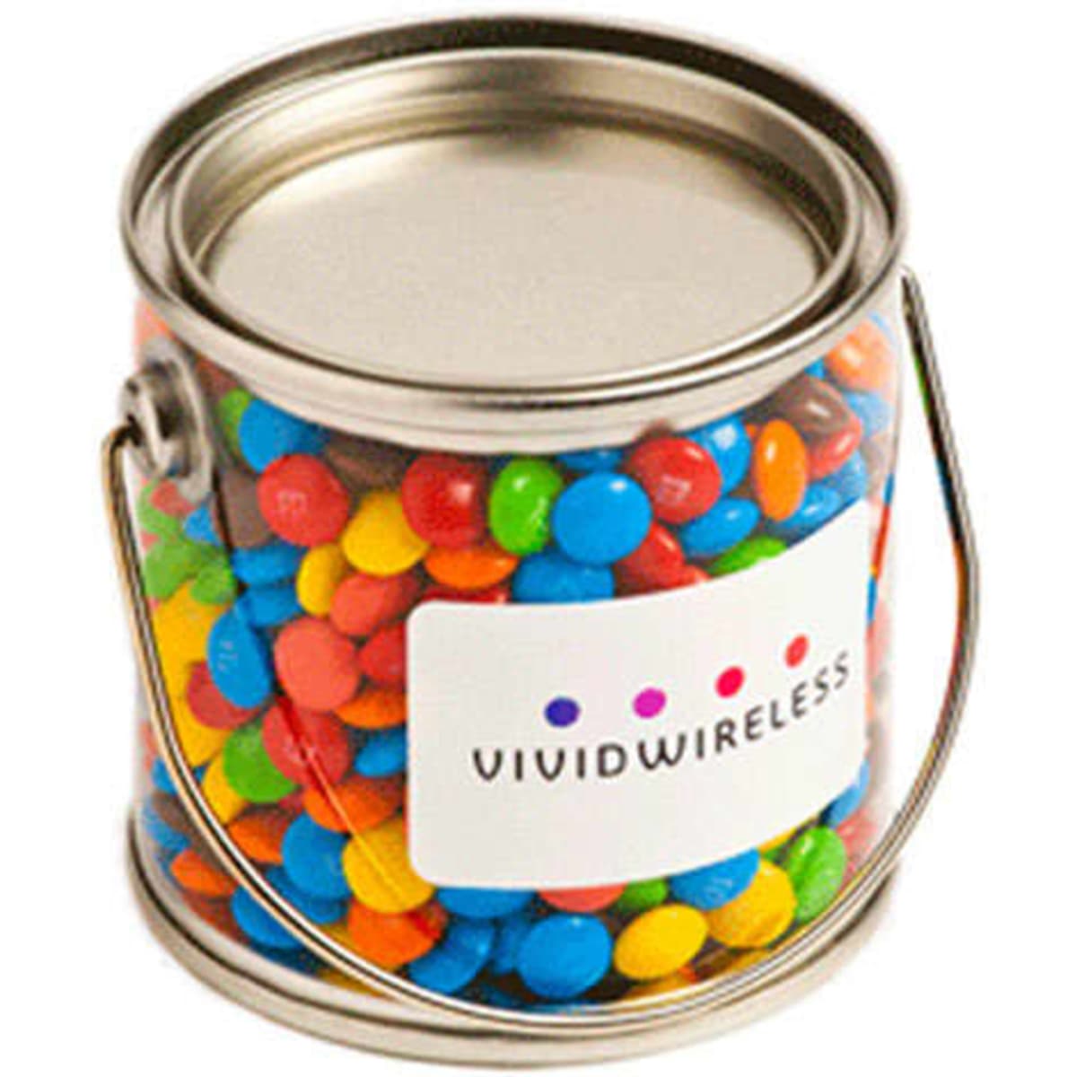 A small clear PVC bucket filled with colourful mini M&Ms, featuring a silver metal lid and handle.