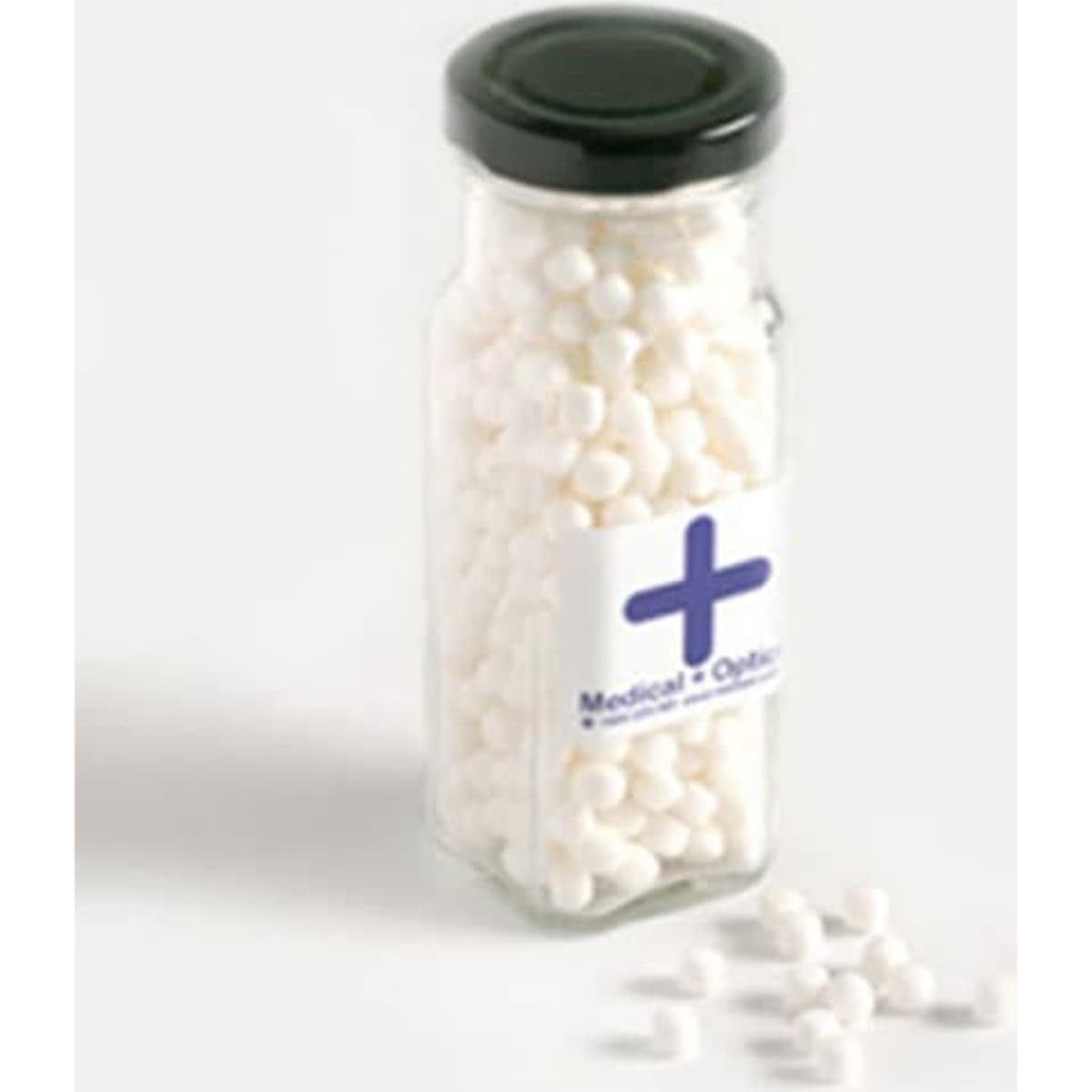 A tall glass jar with a black lid filled with white mints, partially spilled onto a light background.