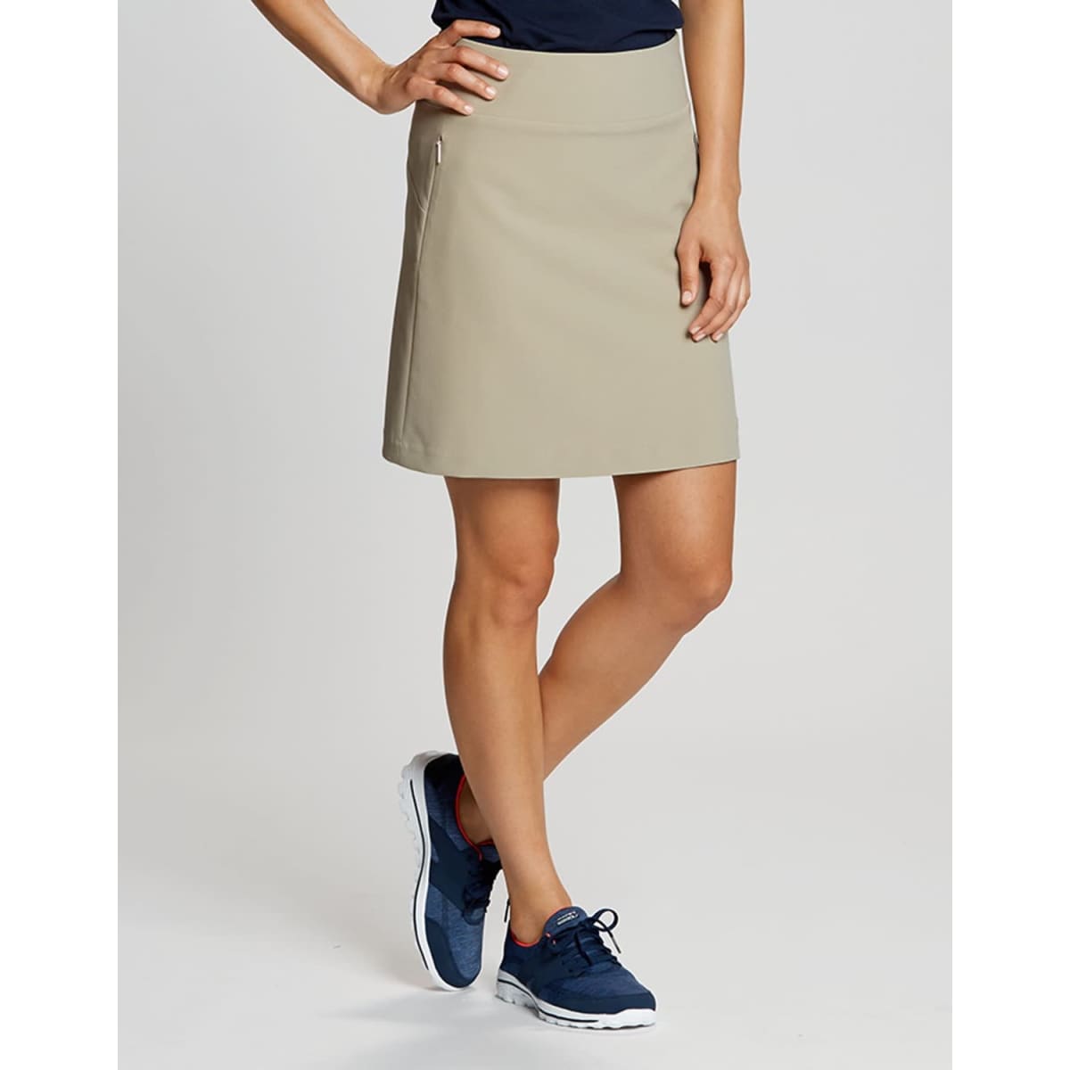 A beige pull-on skort featuring a sleek design and a side zip pocket, worn with casual athletic shoes.