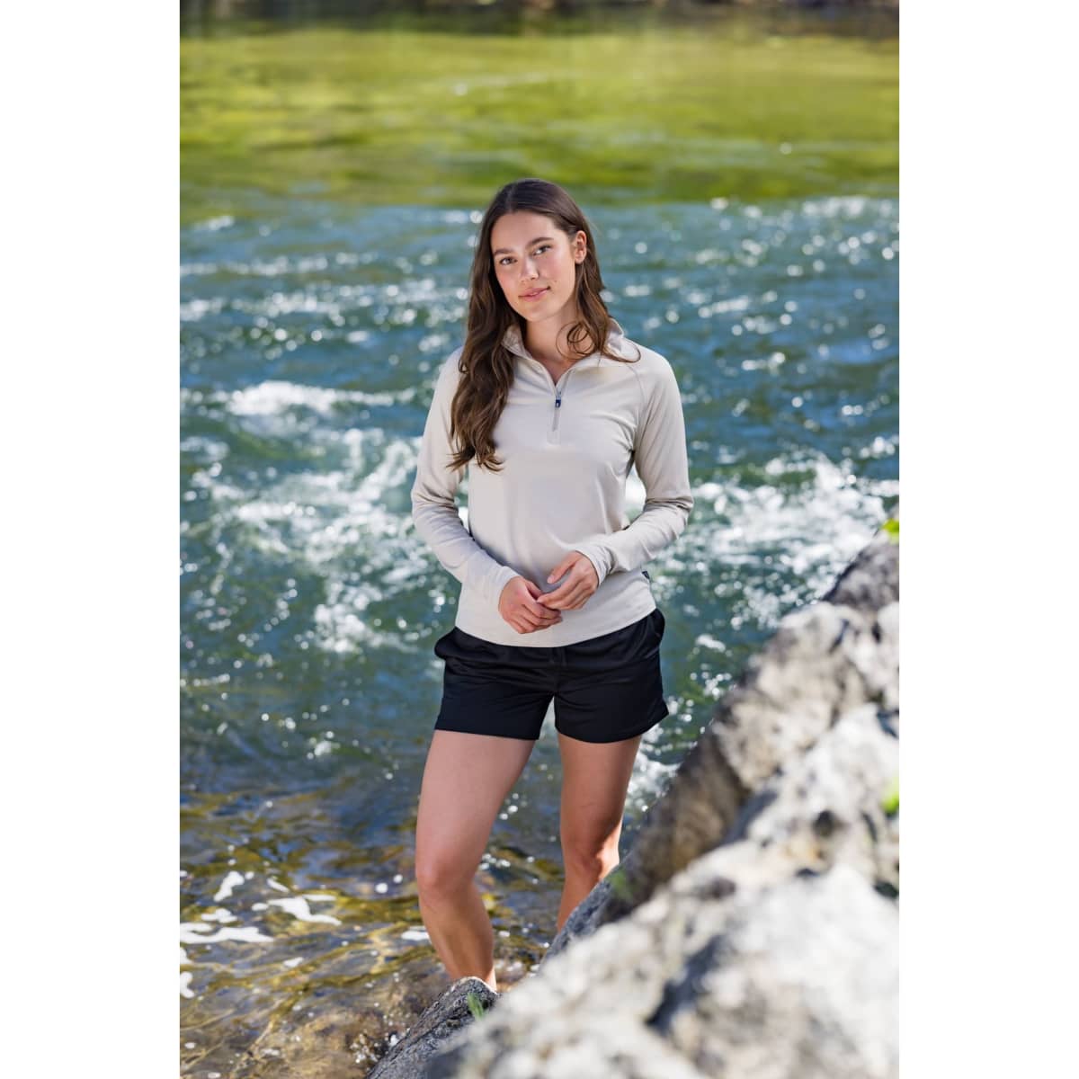 A lightweight, beige quarter zip pullover paired with black shorts, set against a natural water background.