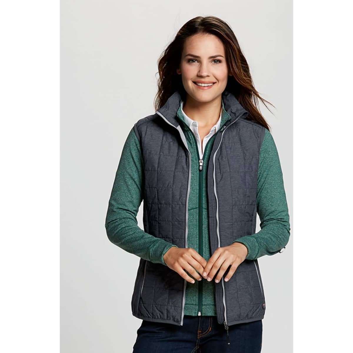 A woman wears a grey puffer vest over a green top, featuring a branding logo on the vest.