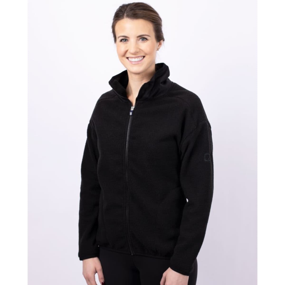 A woman wearing a black eco Sherpa jacket with a zip-up front and a stand collar. The jacket has a logo on the sleeve.