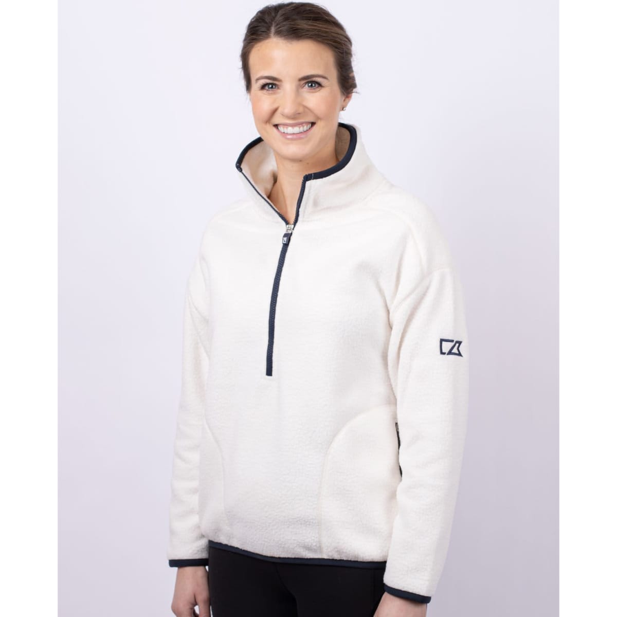 A white eco sherpa half zip jacket with a navy zipper and a logo on the sleeve, worn by a smiling person.