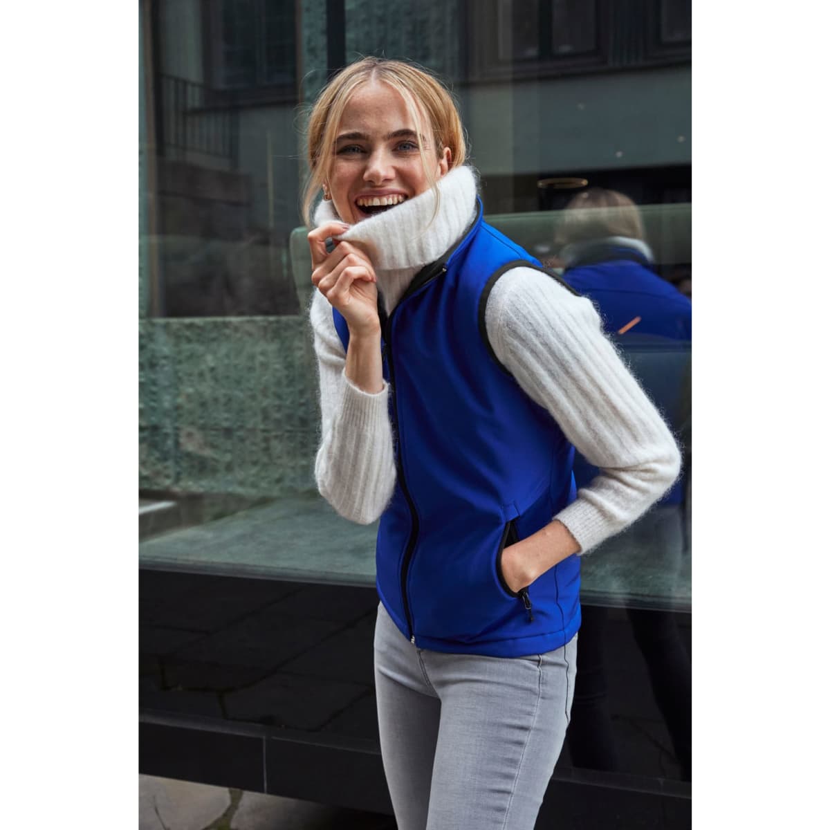 A blue softshell vest worn over a light sweater, featuring a high collar and a zip front, with a logo on the chest.