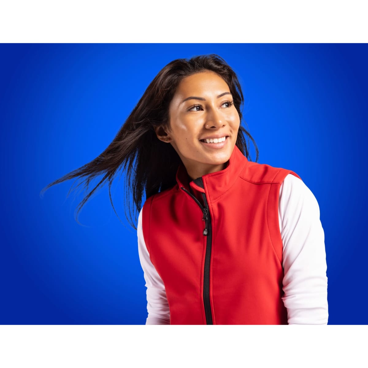 A woman wearing a red eco stretch vest with white sleeves, set against a blue background. The vest features a logo.