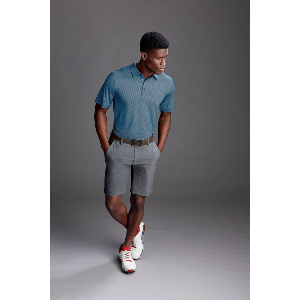 A pair of grey sports shorts, styled with a blue polo shirt and white sneakers, featuring a logo on the shorts.