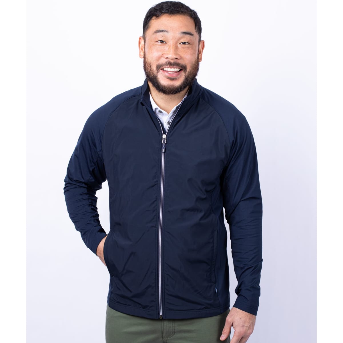 A man wearing a navy blue full zip jacket with a zippered front and a logo. The jacket features long sleeves.