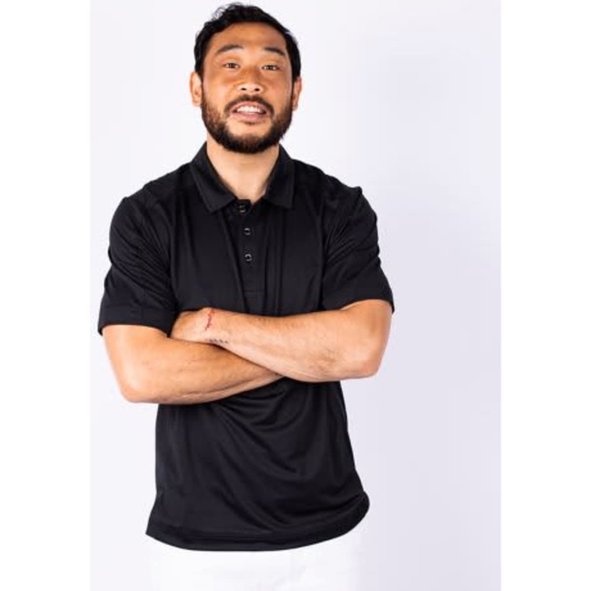 A man wearing a black polo shirt, standing with arms crossed and smiling, with a plain white background.