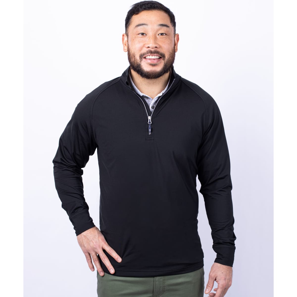 A man wearing a black half zip jumper with a collar and a logo on the chest.