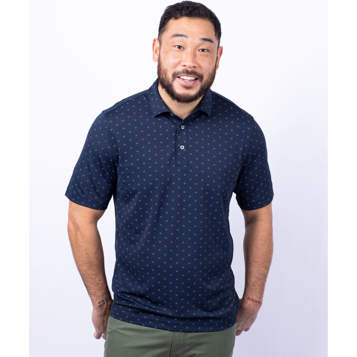 A man is wearing a men's navy polo shirt with a tile print pattern and a logo on the chest.