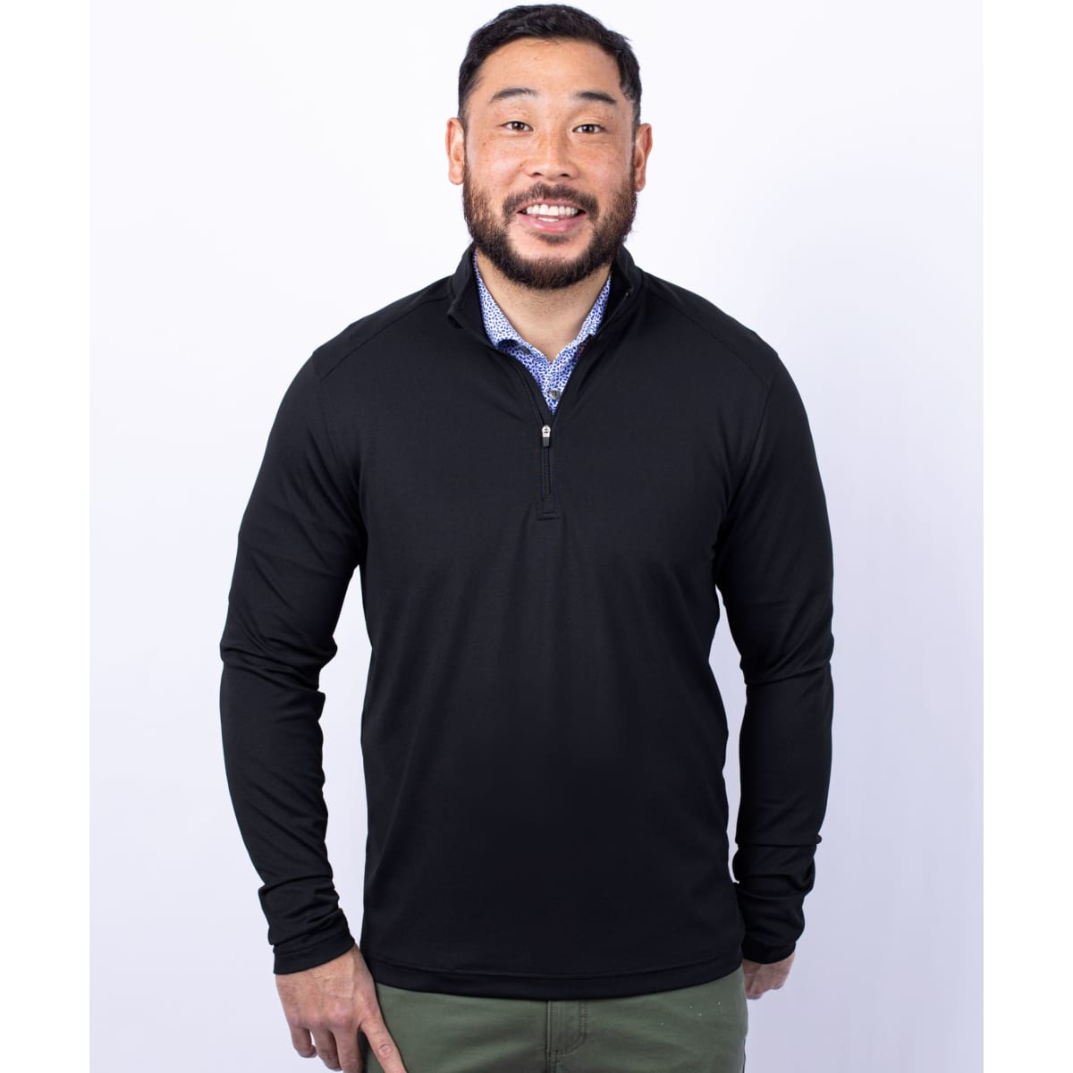 A man is wearing a black half-zip jacket with long sleeves and a logo on the chest.