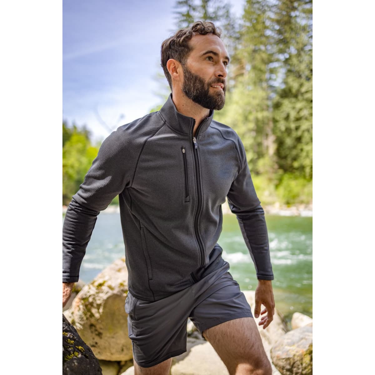 Men’s Peshastin Eco Fleece full zip jacket in dark grey, featuring a front zip pocket, set against a natural river backdrop.