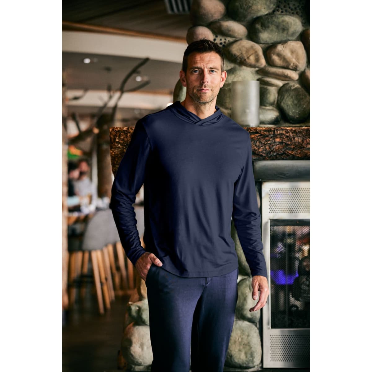 A men's hooded shirt in navy blue, featuring a relaxed fit and long sleeves, displayed indoors near a stone fireplace.