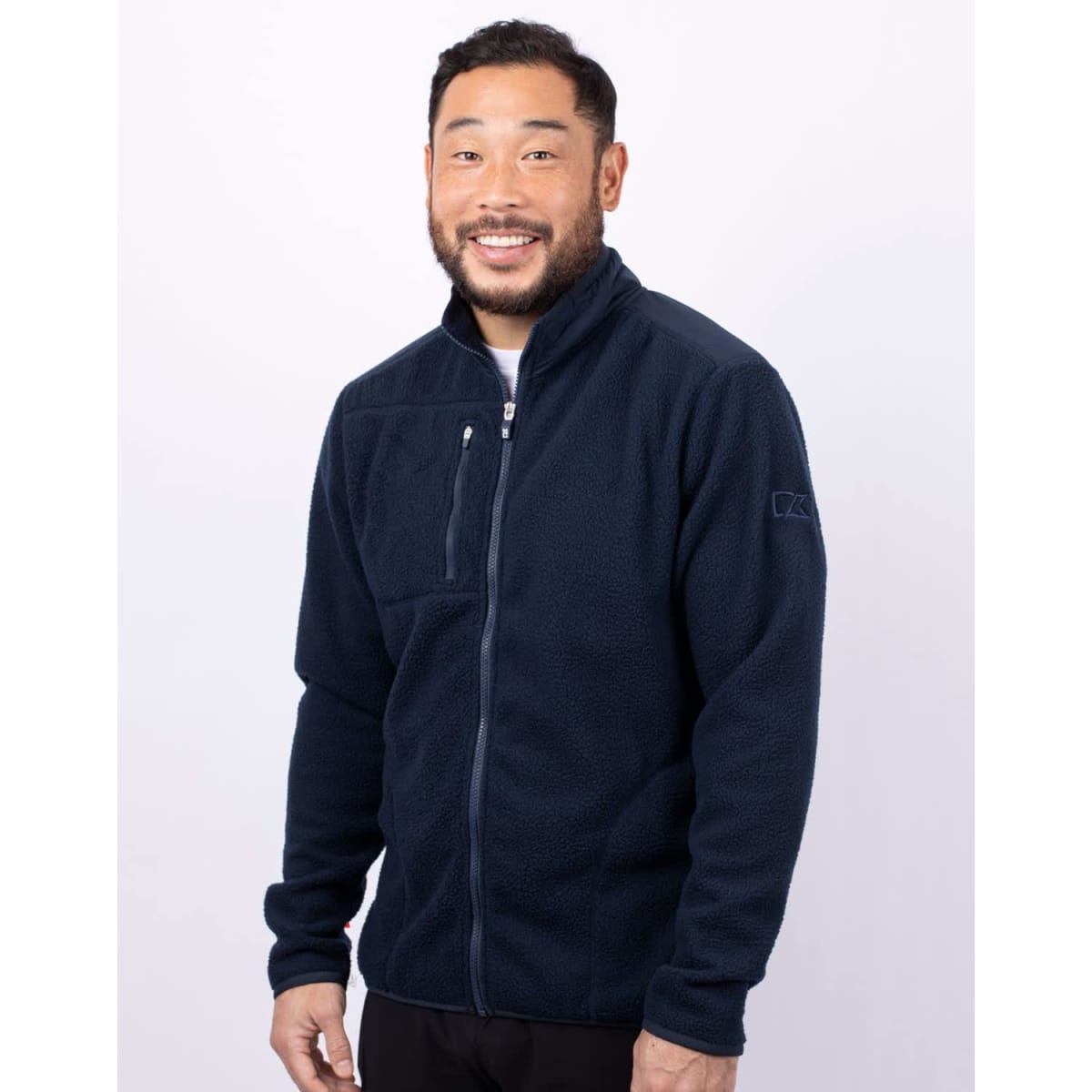 A man wearing a navy blue eco Sherpa jacket with a zippered front and a logo on the sleeve.