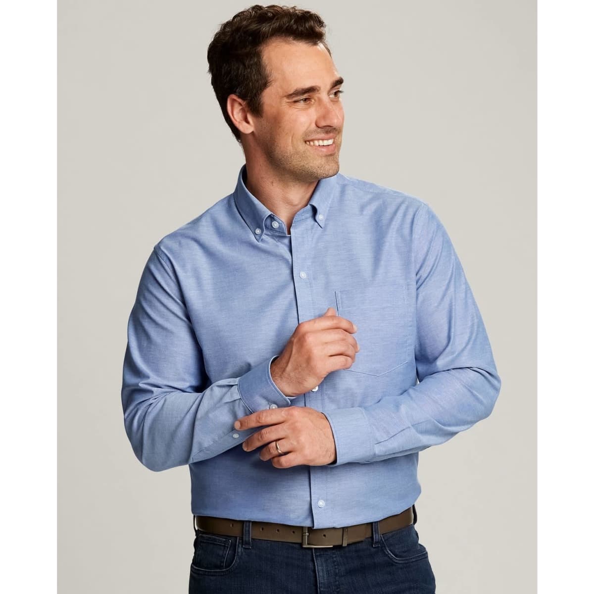A light blue button-up shirt is worn by a smiling man. The shirt features a collar and has a logo.