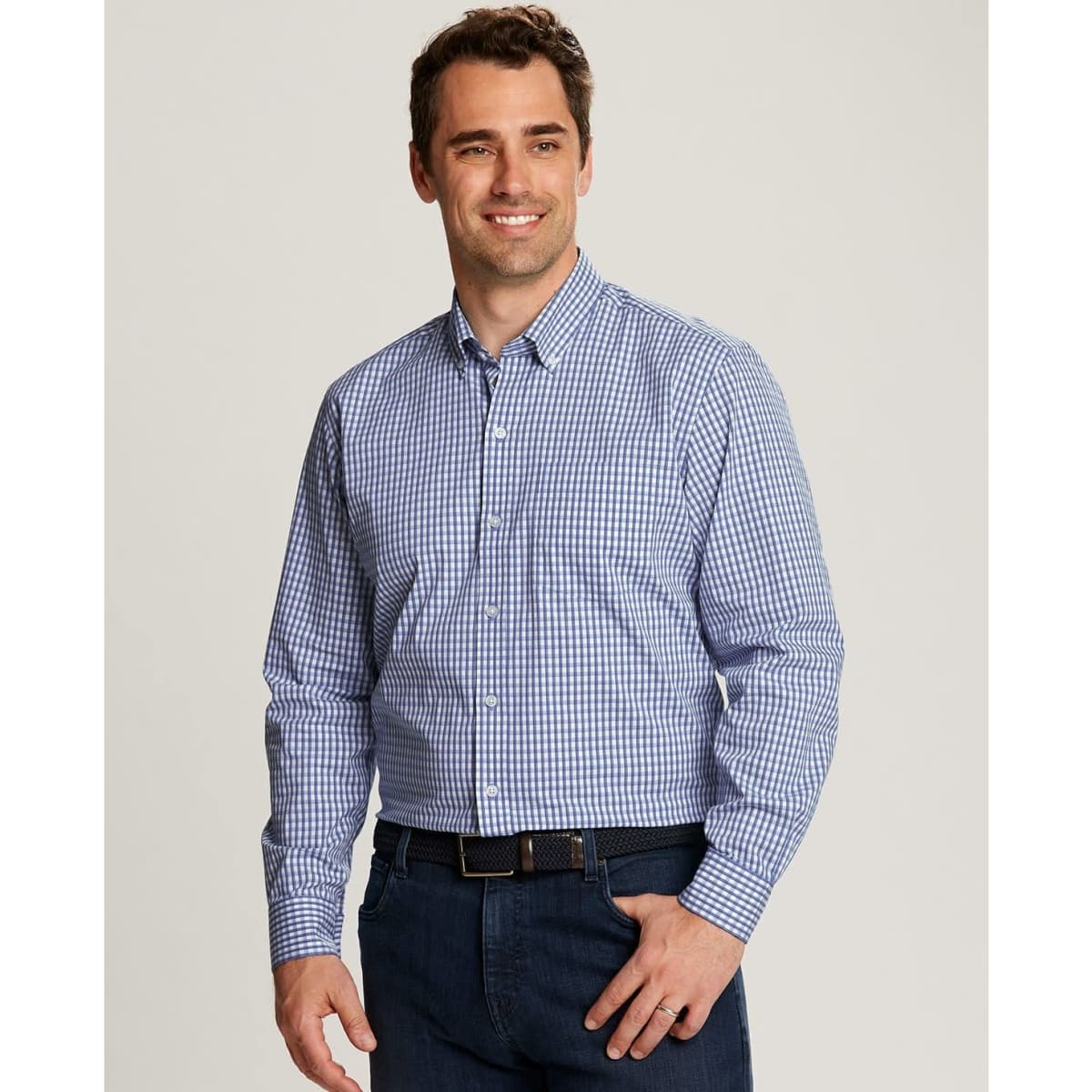 A man wearing a blue and white gingham button-up shirt, smiling. He is styled with a casual look.