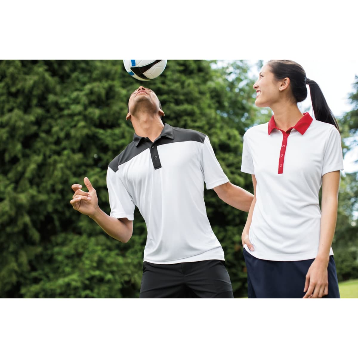 A male and female model wearing men's polo shirts in white with black and red colourblock accents, featuring a logo.