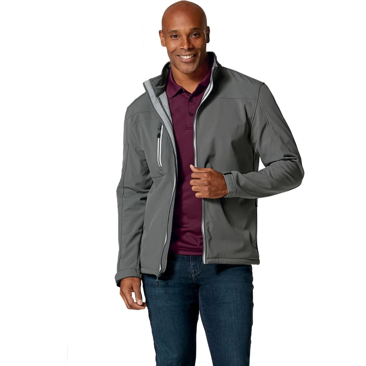 A man models a grey softshell jacket with a zippered pocket and a logo on the chest. He wears a purple polo underneath.