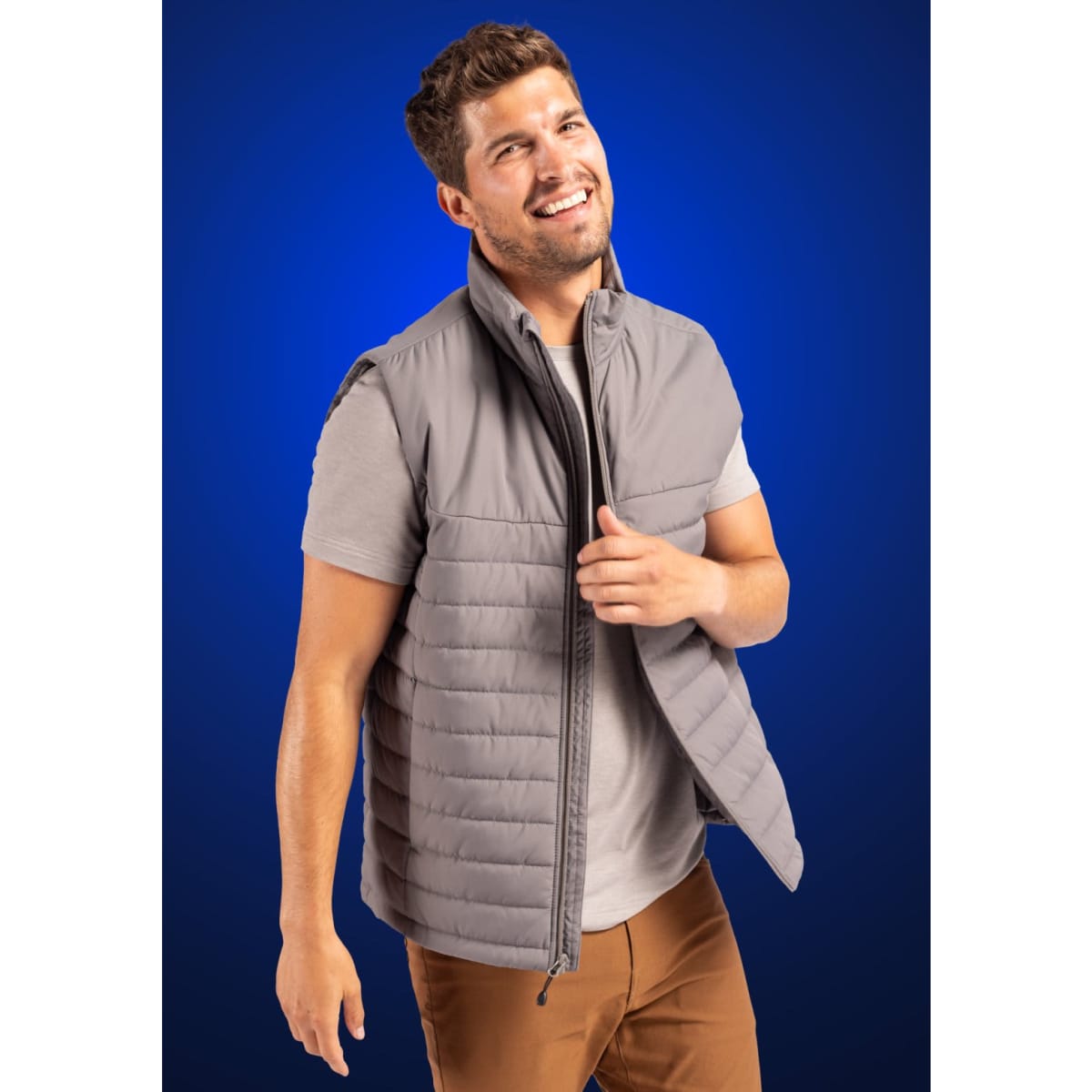 A grey puffer vest with a zip front and a simple design, modelled by a smiling man against a blue background.
