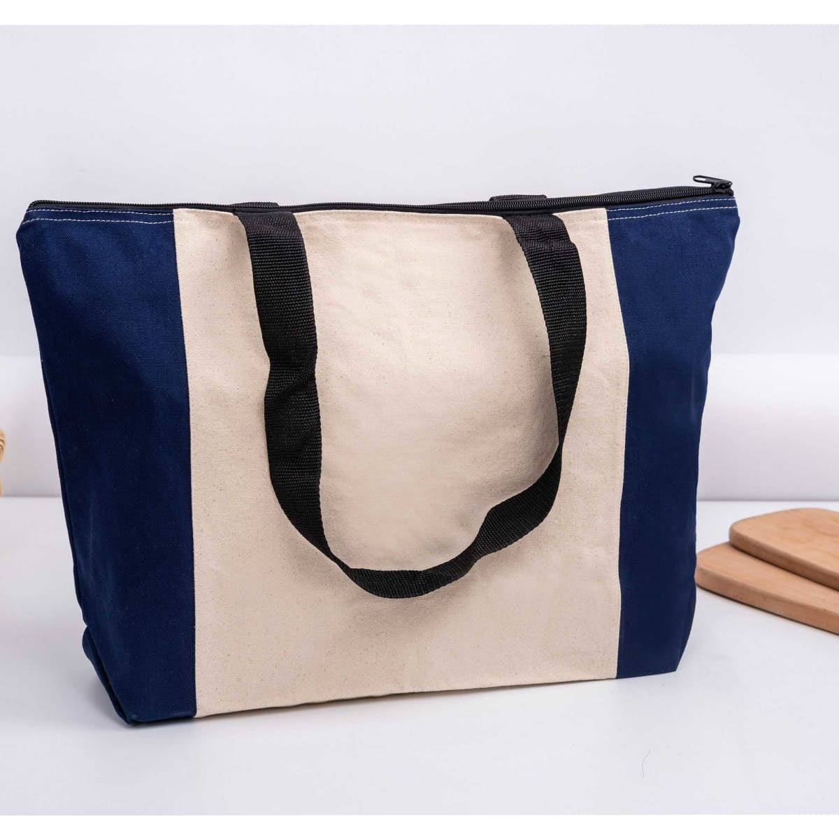 A tote bag featuring a cream and navy colour scheme, with black handles and a zip closure. It has branding on it.