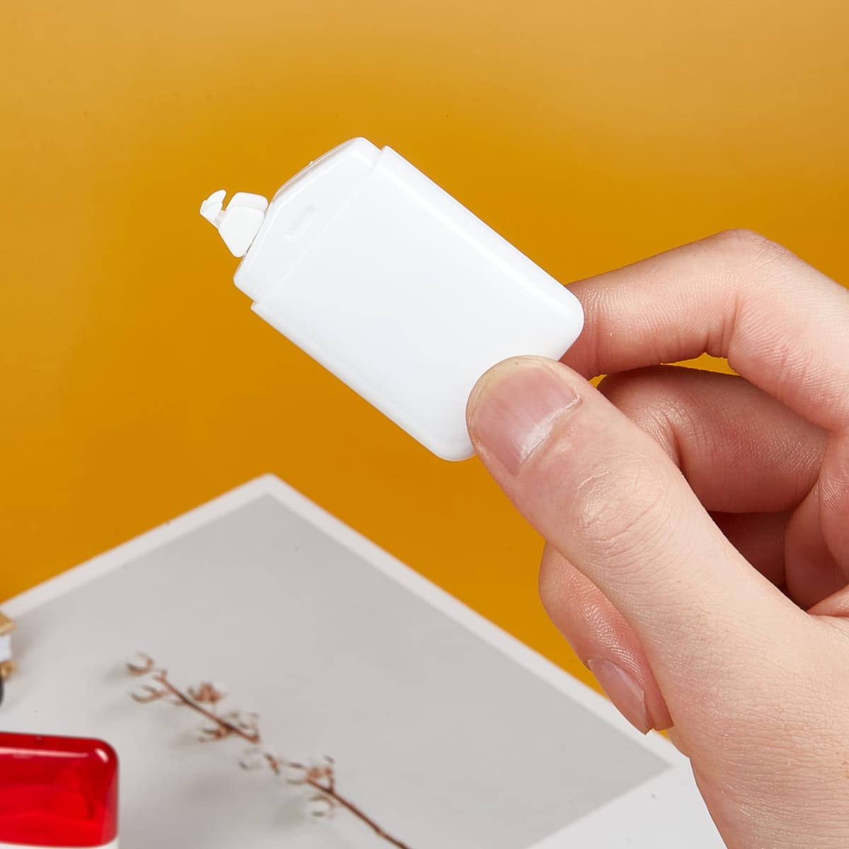 A white correction tape dispenser held in a hand, against a vibrant orange background.