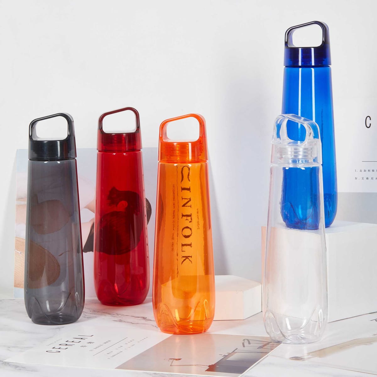 A drink bottle display featuring five translucent bottles in red, orange, blue, grey, and clear, each with a handle and logo.