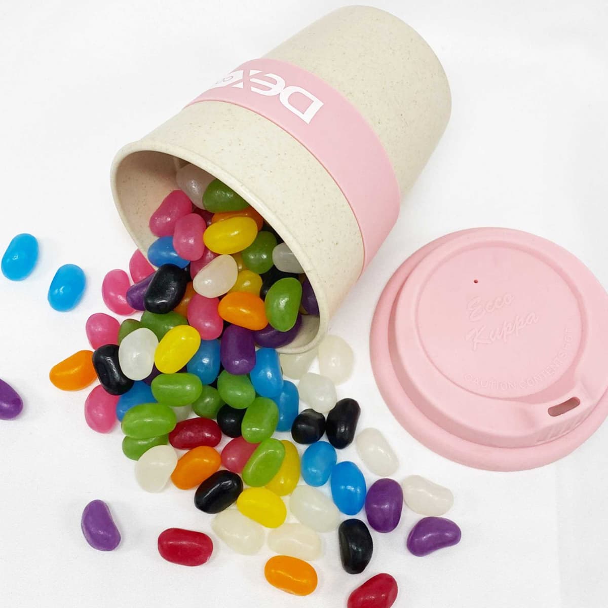 A bamboo cup in light pink filled with colourful jelly beans, with some beans spilled outside the cup.