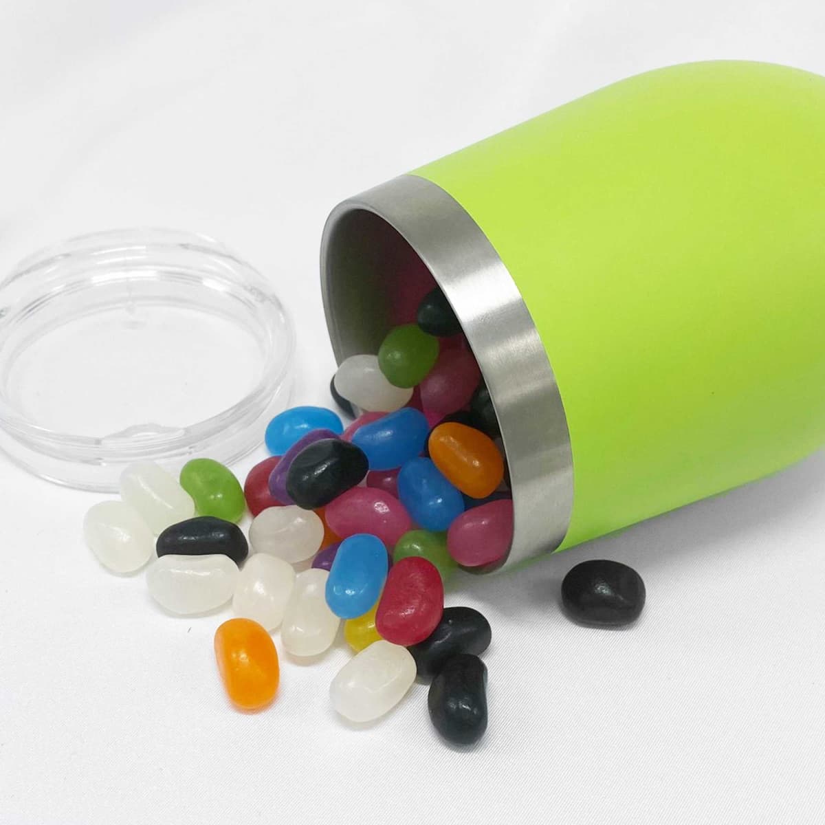A green coffee cup with a stainless steel rim tipped over, spilling various coloured jelly beans.