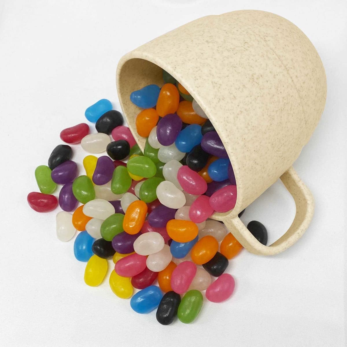 A reusable coffee cup made from wheat straw, surrounded by a variety of colourful jelly beans spilling out.