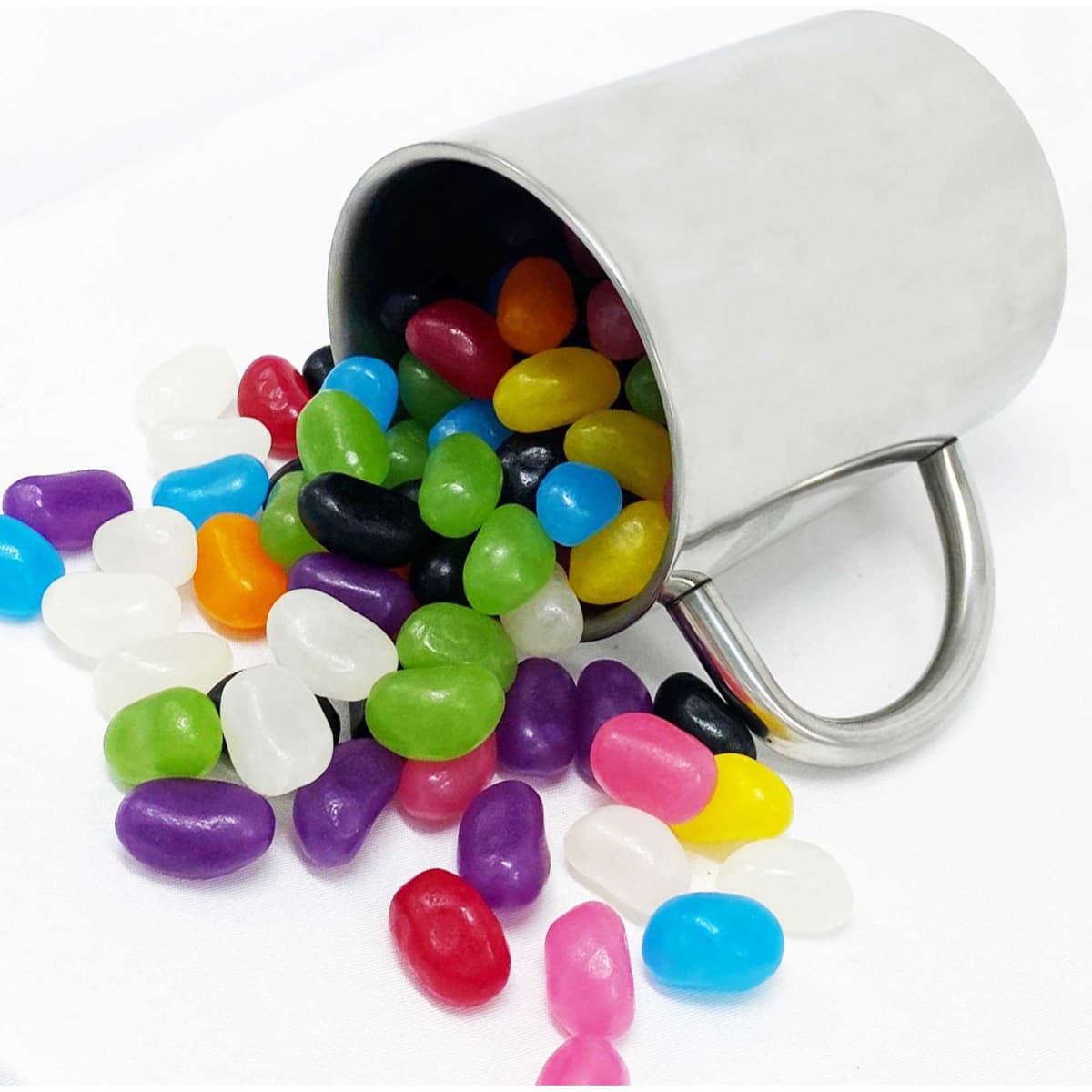 A stainless steel mug tipped over, spilling an assortment of colourful jelly beans in various shades.
