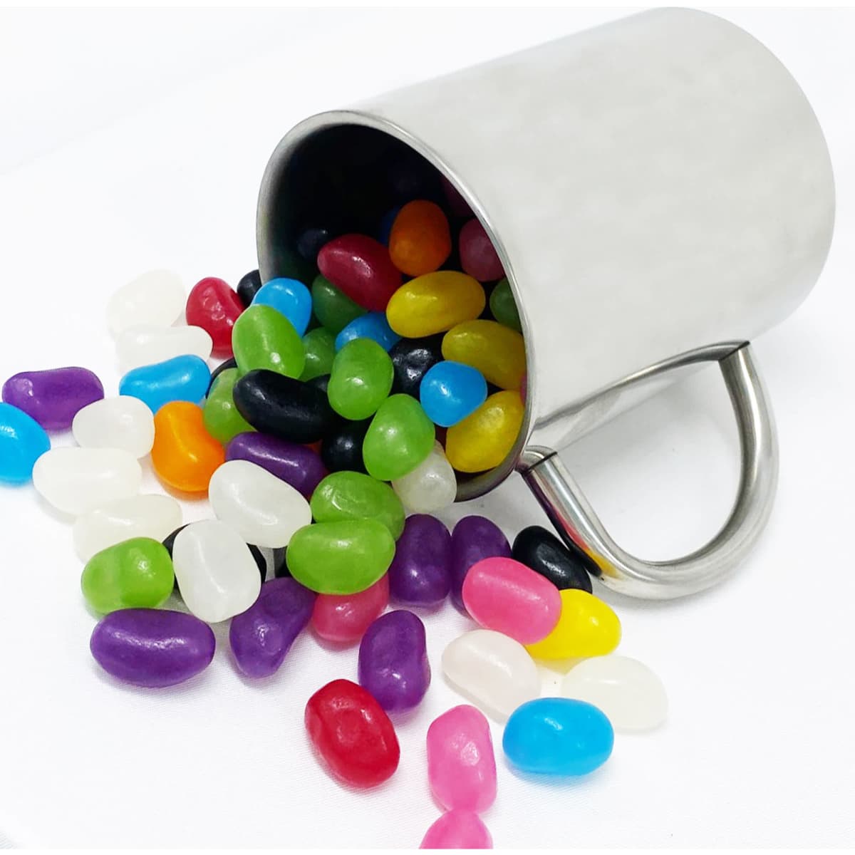 A stainless steel mug tipped over with colourful jelly beans spilling out in various shades.