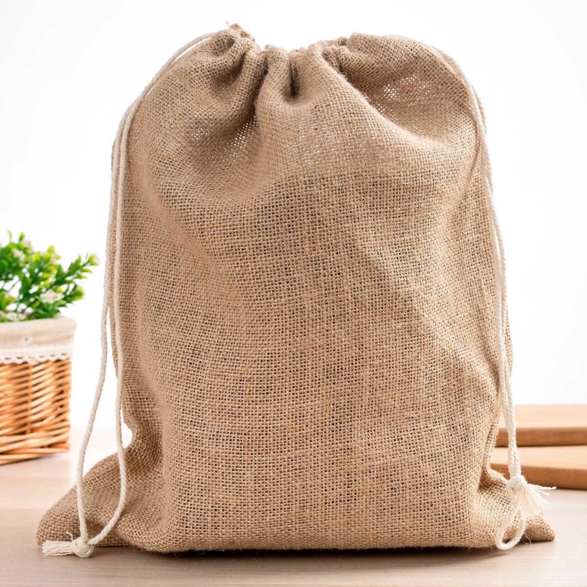 A natural jute bag with a drawstring closure, featuring a textured surface and cream-coloured cords.