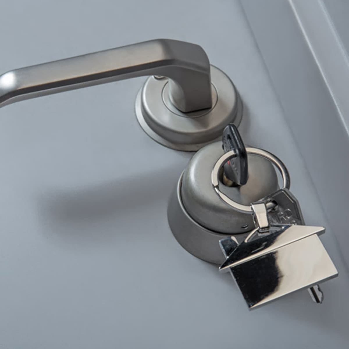A silver house-shaped key ring attached to a silver door handle, set against a grey background.