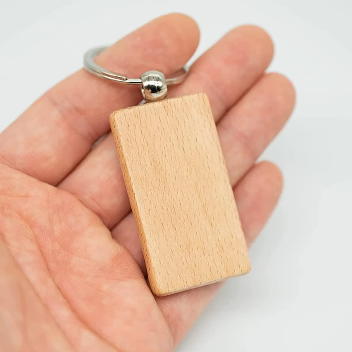 A wooden keyring with a rectangular wooden tag attached to a silver keyring, held in a hand.