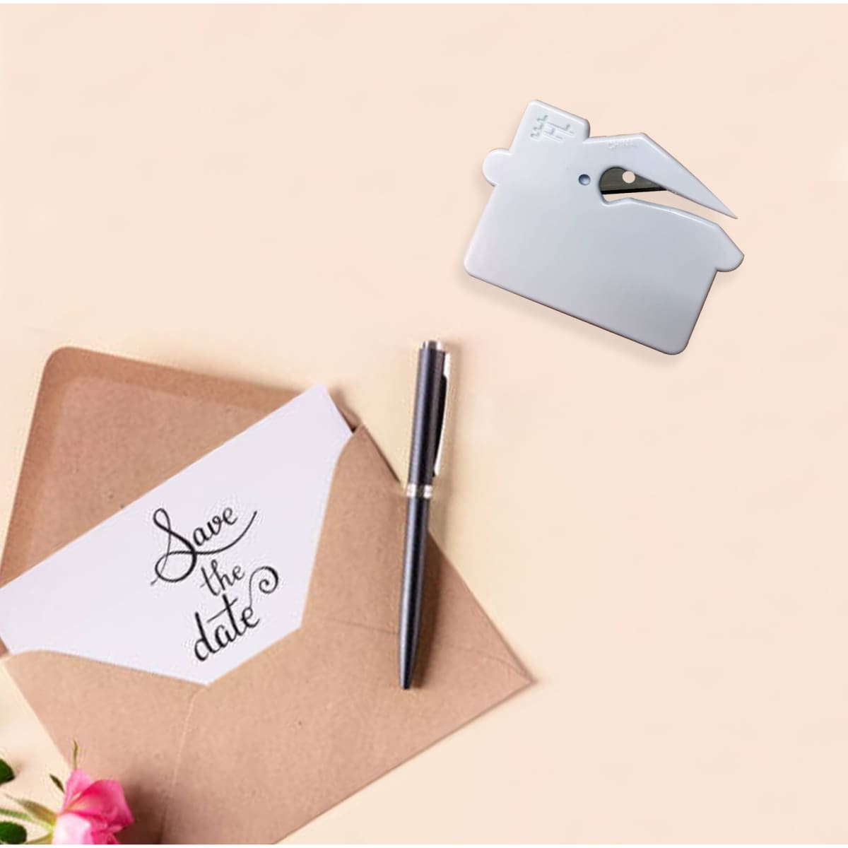 A silver house-shaped letter opener placed near an envelope and a pen, set against a soft background with flowers.