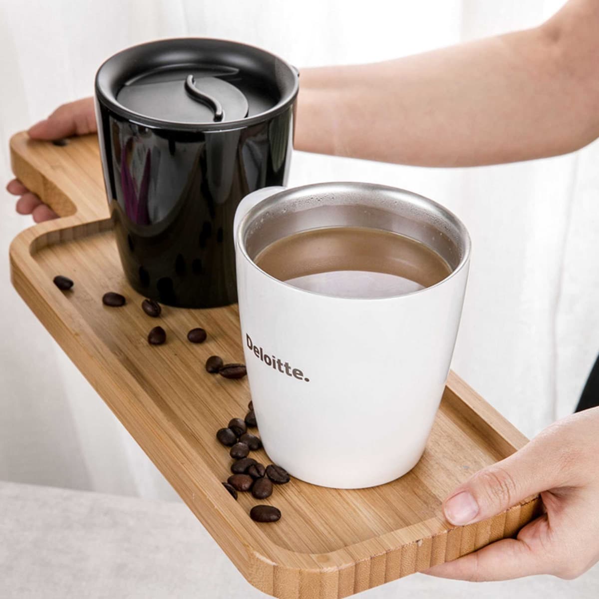 A drinkware set featuring two coffee mugs, one black and one white, on a wooden tray with coffee beans.