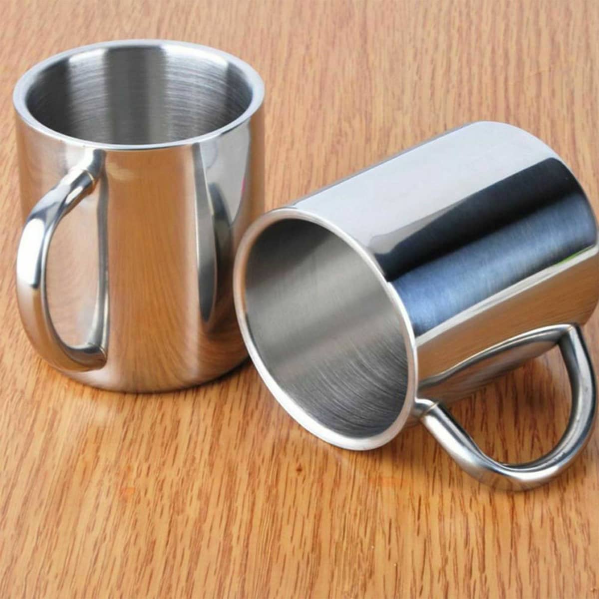 A set of stainless steel coffee mugs with a shiny finish, featuring curved handles, placed on a wooden surface.