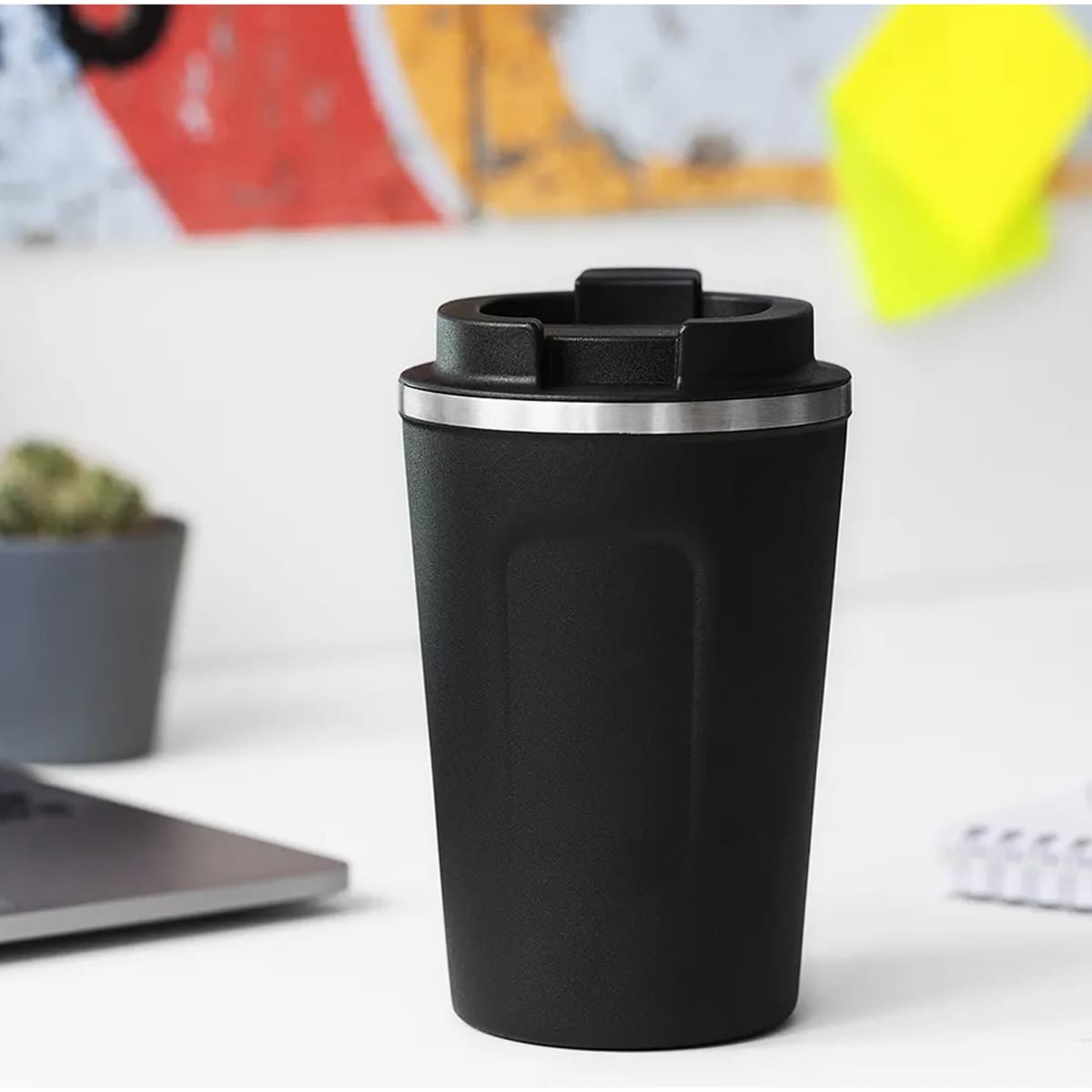A black reusable coffee cup with a silver band at the top, featuring a lid and a glossy finish.