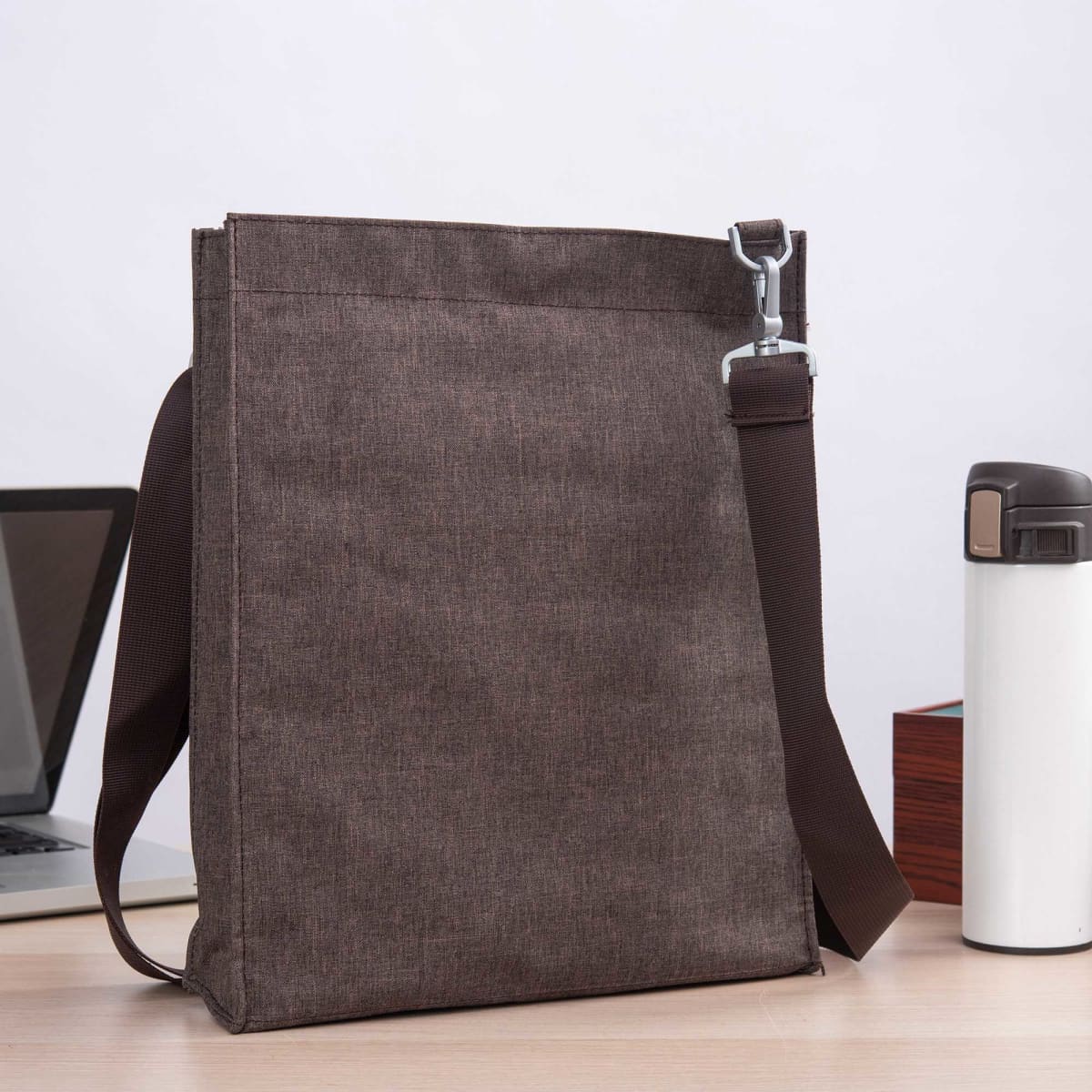 A brown nylon library bag with a shoulder strap, placed beside a laptop and a drink bottle on a table.