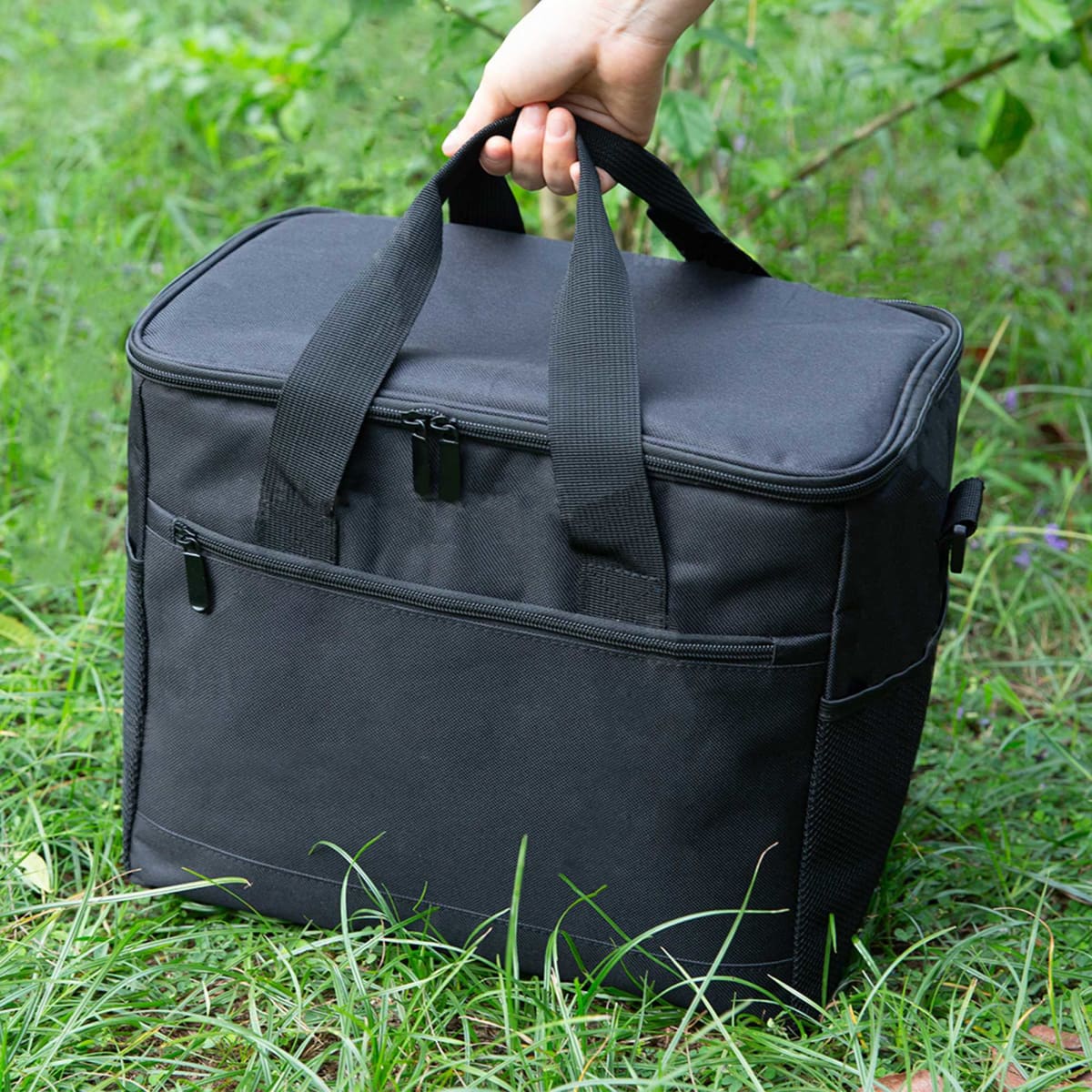 A black large nylon cooler bag with dual handles and a front pocket, set against green grass.