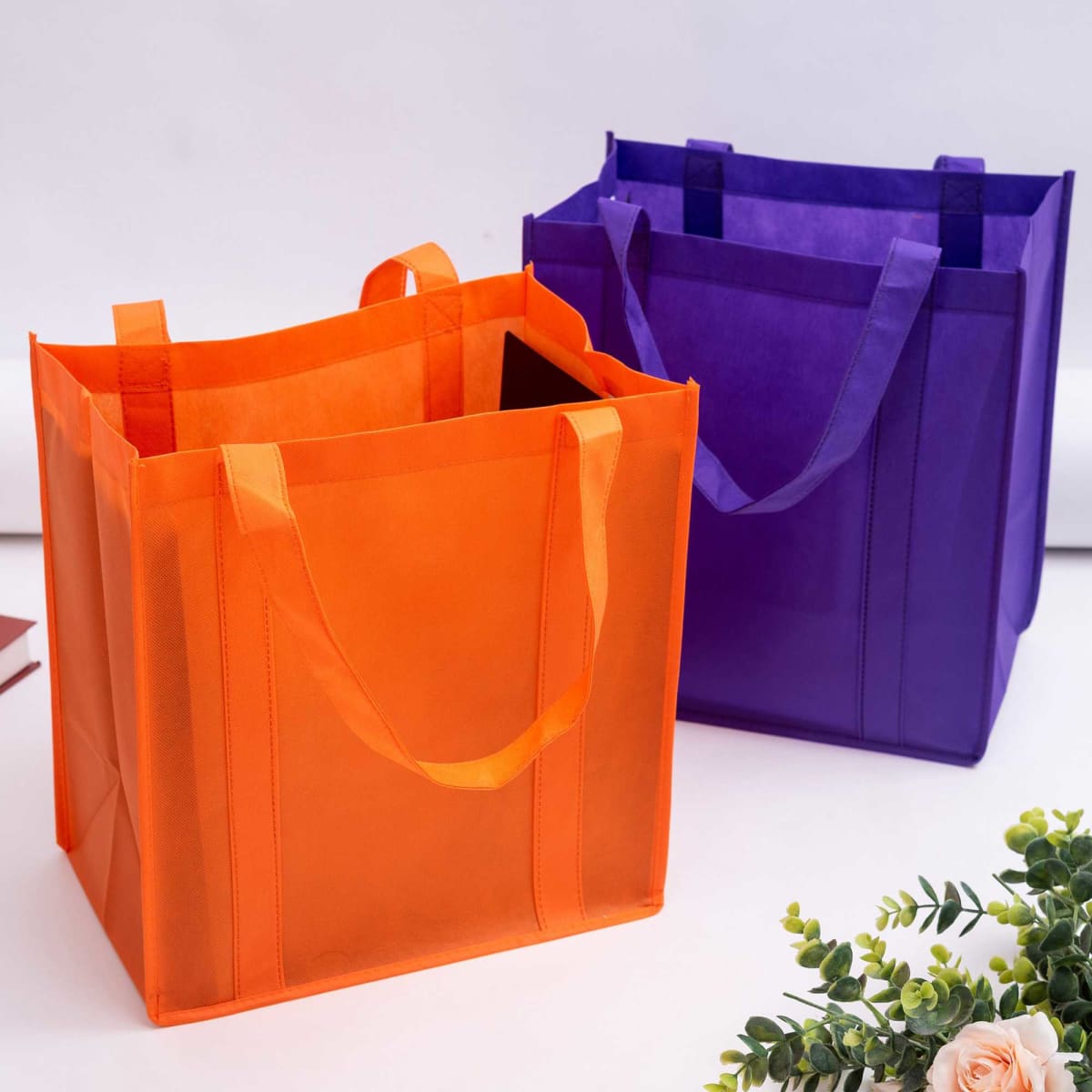 Two reusable non-woven shopping bags in orange and purple, featuring handles and a simple design.