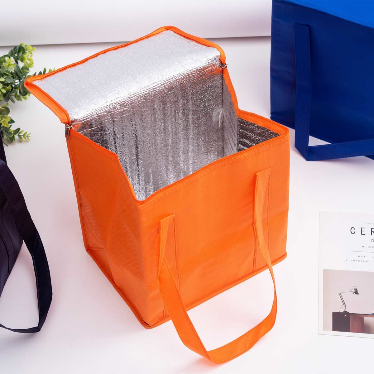 An orange non-woven cooler bag with a zipped lid and insulated interior, featuring two handles.