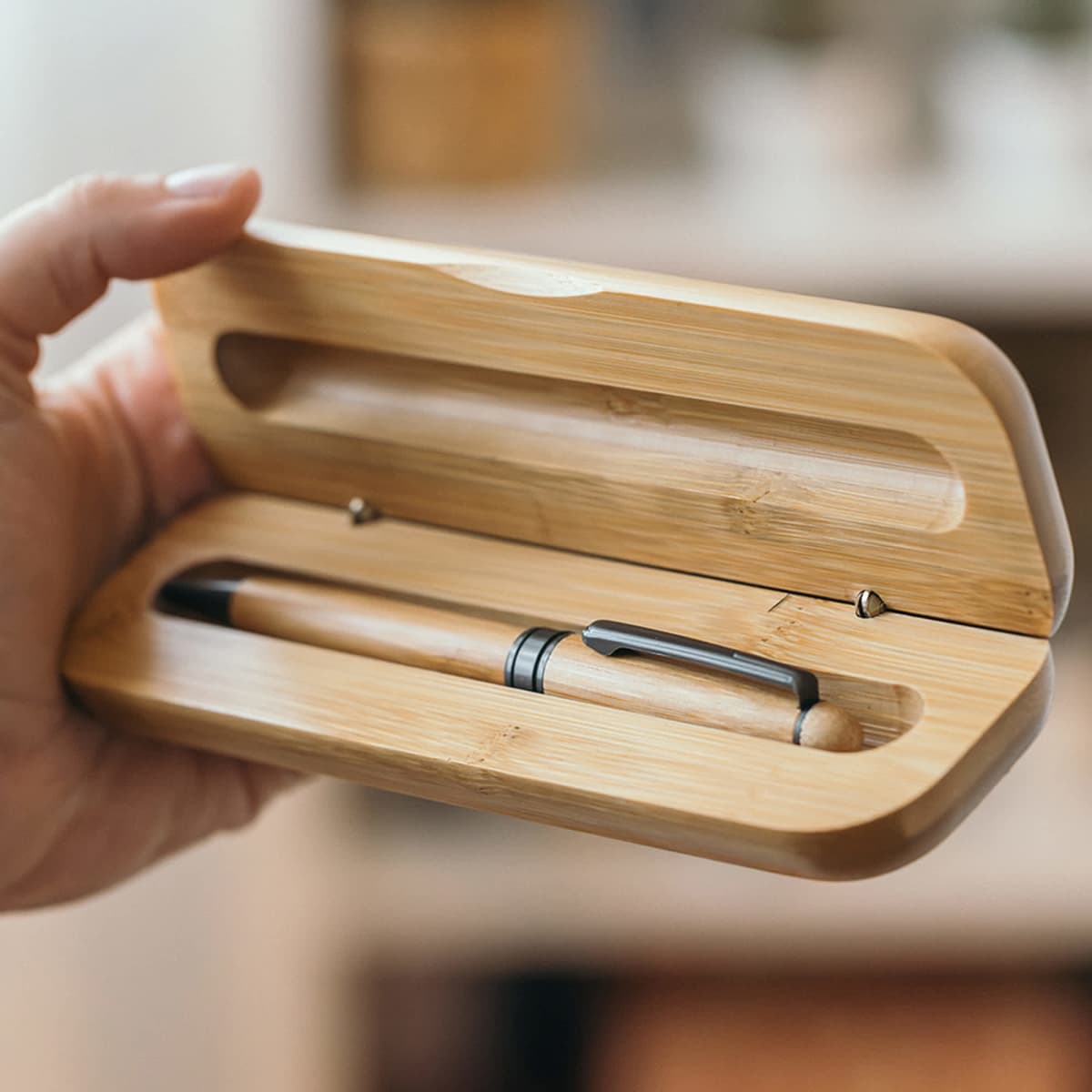 A bamboo pen case holding a wooden pen with a silver clip, featuring a natural finish. The case and pen are co-ordinating in colour.